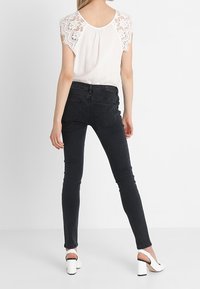 White blouse with lace cap sleeves paired with fitted black jeans, featuring a smooth texture and a slim silhouette. White high-heeled shoes.