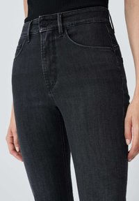 Jeans en denim noir taille haute, avec un design classique à cinq poches et des coutures discrètes. Le tissu a une texture lisse.