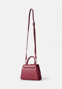 Borsa a tracolla in pelle cremisi con una forma triangolare strutturata, manico corto in alto e tracolla regolabile. Texture liscia, hardware minimale.