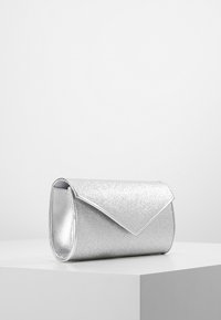 Srebrny błyszczący kopertówka o usztywnionym kształcie, z metaliczną powłoką i gładką fakturą. Zaokrąglone krawędzie i zapięcie na klapę.