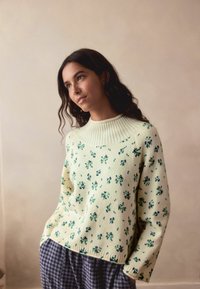 Kootud sweater helekollases toonis, millel on soonik krae ja lilleline muster rohelises ja sinises. Soe tekstuur, lõdva istuvusega, pikad varrukad.