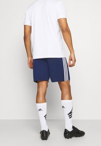 White short-sleeve shirt, navy shorts with white stripes, white knee-high socks with black accents, and black soccer cleats.