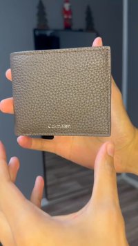 Graue Lederbrieftasche mit Textur und rechteckiger Form, mit einem silbernen "Calvin Klein"-Logo auf der Vorderseite und minimalistischem Design.