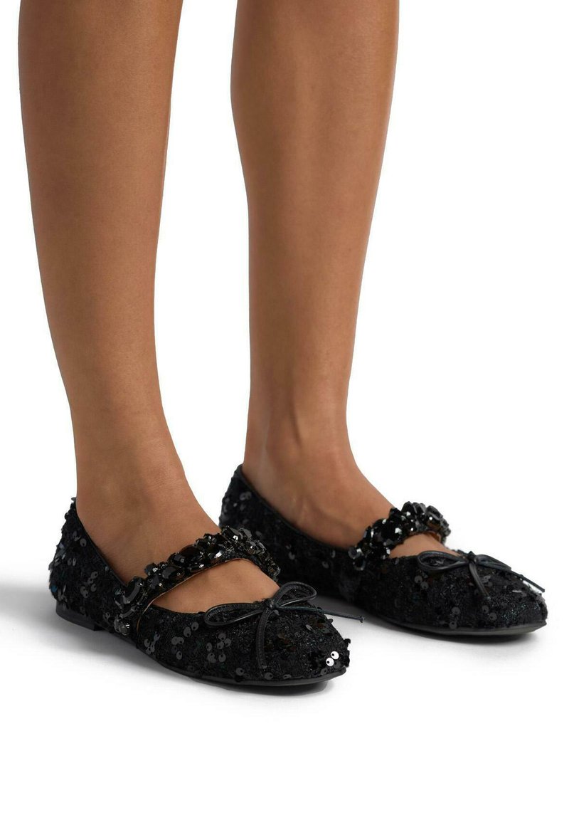 Ballerine nere in paillettes con punta arrotondata, dotate di una fascia decorativa con perline e un fiocco nella parte anteriore. Suola piatta, superficie strutturata.