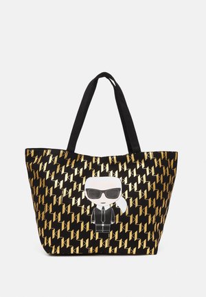 Borsa a tracolla nera con un motivo geometrici dorati e un personaggio dei cartoni animati che indossa occhiali da sole e un completo sul davanti. Manici neri.