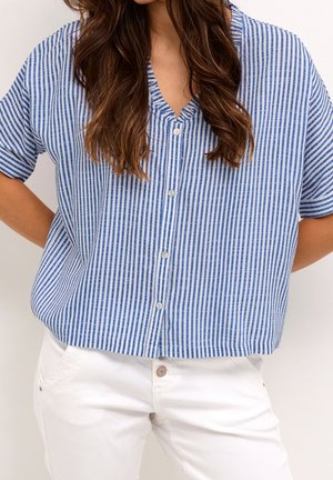 Chemise à rayures bleues et blanches, à manches courtes, avec un col en v et une coupe décontractée. Pantalons blancs visibles, avec un détail de bouton apparent.