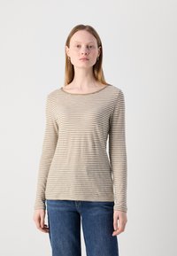Beige, hosszú ujjú felső vékony barna csíkokkal, kerek nyakkivágással és puha anyagból. Kék farmernadrággal párosítva, amely laza szabású.