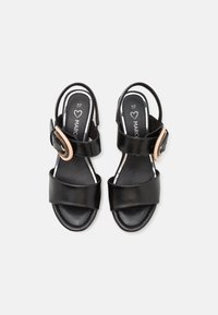 Sandali in pelle nera con doppie cinghie, fibbia regolabile e suola piatta. Presentano una texture liscia e un design aperto sul retro. Etichetta della taglia visibile.