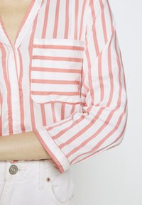 Maglietta a righe in rosa chiaro e bianco, con tasca, scollatura a V e maniche arrotolate, realizzata in tessuto leggero.