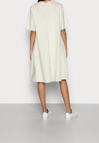 Vaaleanvihreä, lyhythihainen mekko, jossa on rento muotoilu ja pyöreä pääntie. Pehmeä kangas ja kerroksellinen hame, jota on paritettu valkoisten tennareiden kanssa.