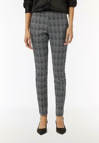 Schwarz-weiße gemusterte Hose mit Zickzack-Design, schlanker Schnitt, mit glatter Stofftextur, kombiniert mit schwarzen spitzen High Heels.