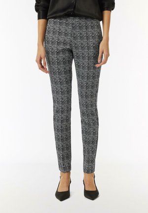 Schwarz-weiße gemusterte Hose mit Zickzack-Design, schlanker Schnitt, mit glatter Stofftextur, kombiniert mit schwarzen spitzen High Heels.