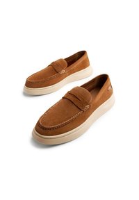 Mocassini in suede marrone con un design cucito, suola piatta in gomma crema, punta arrotondata e una cucitura decorativa lungo la parte superiore.