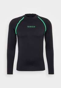 Schwarzes Langarm-Rashguard mit grünen Akzenten. Verfügt über einen hohen Kragen und einen Reißverschluss auf der Rückseite. "Calvin Klein"-Logo in Grün auf der Vorderseite.