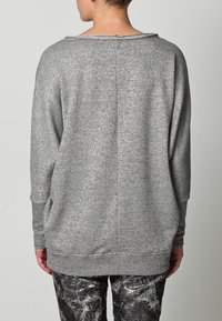Szary dzianinowy sweter typu pulower o luźnym fasonie, z szerokim, zaokrąglonym dekoltem, długimi rękawami i teksturowanym wykończeniem. Ma ozdobne przeszycie na plecach.