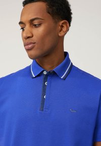 Polo shirt blu realizzato in tessuto testurizzato con un colore uniforme, apertura con due bottoni, colletto a contrasto e piccolo logo sulla parte anteriore.