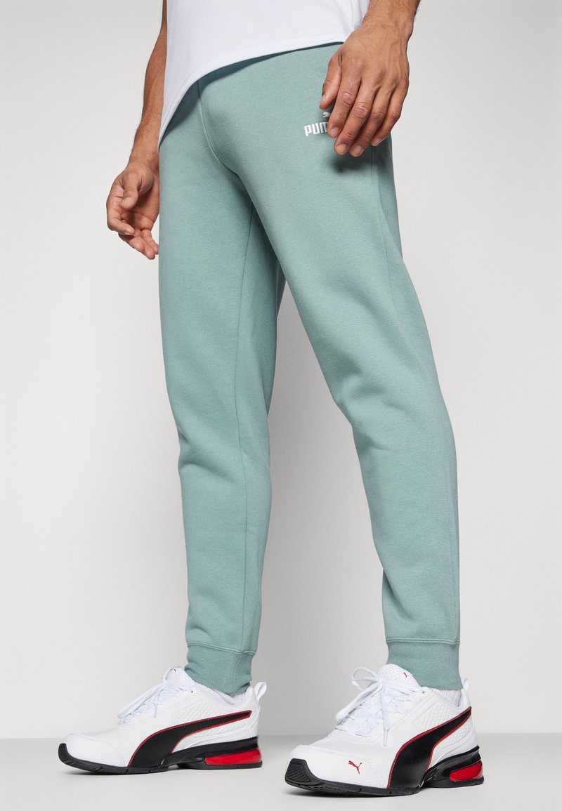 Pantaloni della tuta color turchese chiaro realizzati in morbido tessuto misto cotone, con un design aderente e un piccolo logo bianco sul retro. Abbinati a sneakers bianche e nere.