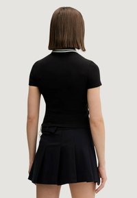 Černé polo tričko s krátkými rukávy a bílými detaily na límci, doplněné černou plisovanou sukní s mašlí a detaily na zip.