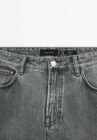 Jean en denim gris avec bouton à l’avant, passants de ceinture et étiquette indiquant la marque Massimo Dutti et le style relaxed fit.