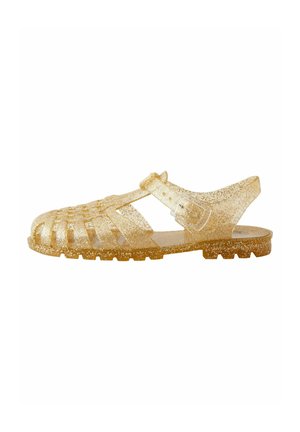 Transparenta guld jellysandaler med dekorativa utskärningar, justerbar rem och texturerad sula. Innehåller glitter överallt för extra detaljer.