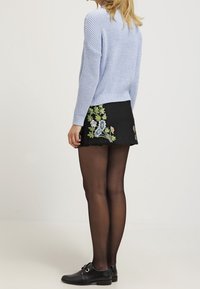 Suéter de punto azul claro, falda negra bordada con diseño floral, medias negras transparentes y zapatos negros con tira y hebilla.