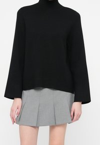 Suéter negro de punto con cuello alto y mangas largas, con un ajuste relajado y un dobladillo que se curva ligeramente hacia arriba. Combinado con una falda plisada gris.