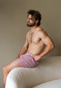 Pantaloni corti a righe rosse e bianche con una vita elastica, indossati da un modello maschile seduto con un fisico muscoloso, su uno sfondo neutro.