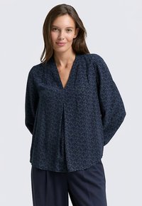 Blouse bleu marine à encolure en V, manches longues et motif abstrait subtil ; fabriquée en tissu lisse avec une coupe décontractée et un détail plissé.
