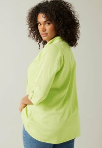 Camicia verde lime con colletto e maniche a tre quarti, caratterizzata da una vestibilità rilassata e un orlo leggermente curvo.