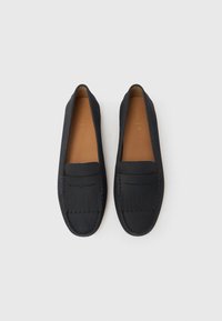 Par crnih kožnih mokasina sa prošivenim detaljima i resama na prednjim panelima, gledano odozgo na svijetloj pozadini.