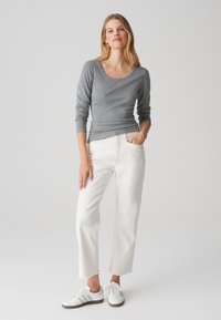 Grijze lange mouwen shirt met een ronde hals, gecombineerd met witte cropped jeans. Witte sneakers maken de outfit af. Glad textuur zichtbaar.