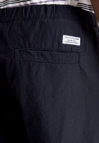 Marineblauwe shorts met een zachte textuur, voorzien van een elastische tailleband en een achterzak. Het label zegt "Maro O'Polo Denim."