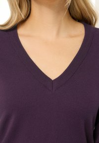 Syvopukoinen villapaita syvän purppuran värissä, pehmeästä neuloksesta valmistettu, jossa on siisti kaula-aukko ja sileä pinta.