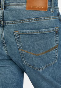 Lichtblauwe denimspijkerbroek met een bruine leren patch met het label "pierre cardin." Kenmerkt zich door twee achterzakken met contrasterende stiksels en een gebogen ontwerp.