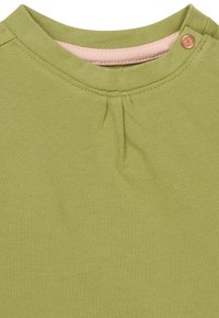 Hellgrünes Baumwoll-T-Shirt mit einem runden Ausschnitt und einer pinken Innenseite, einer dekorativen Falte am Ausschnitt und einem einzelnen Verschlussknopf.