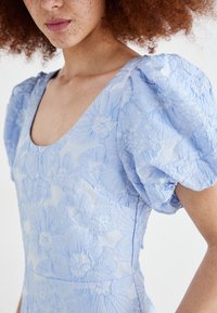 Light blue dress with textured floral pattern, square neckline, and puffed sleeves. Material appears soft with a subtle sheen.