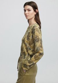 Top de manga larga con un patrón de piel de serpiente amarillo y verde, tejido ligero, escote redondo y un sutil detalle de botón en el cuello.