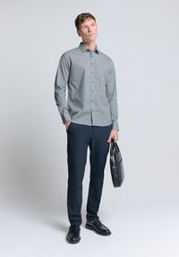 Gekeurde overhemdd blazergroen en wit, gecombineerd met marineblauwe broek en zwarte instappers, met een zwart leren tas. Eenvoudig, op maat gemaakt ontwerp.