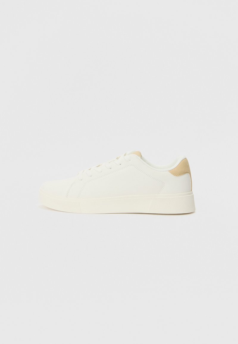 White sneakers with a smooth upper, flat sole, and beige heel patch; features laces and minimal stitching for a clean design.