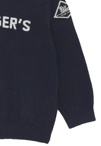 Maglione a maglia blu navy con polsini a coste, scollo rotondo e testo ricamato bianco. Include una toppa triangolare sulla manica.