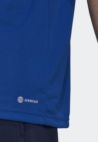 Chemise de sport bleue en tissu lisse qui évacue l'humidité. Présente un logo "AEROREADY" près de l'ourlet, avec une coupe ajustée et des manches courtes.