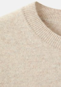 Gebreide trui in een lichte beige kleur met een ronde hals en ribbelboord. De textuur lijkt zacht en iets pluizig.