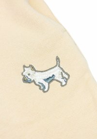 Beige stof met een geborduurd ontwerp van een witte en blauwe hond, met nadruk op gedetailleerde stiksel en een gestructureerd oppervlak.