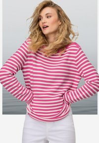 Maglione a righe in rosa e bianco, con maniche lunghe e vestibilità rilassata. Il tessuto sembra strutturato, abbinato a pantaloni bianchi.