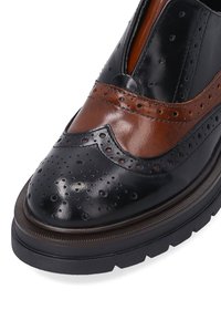 Černá a hnědá kožená bota s brogue detaily, texturovaným povrchem, kulatou špičkou a silnou kontrastní gumovou podrážkou.