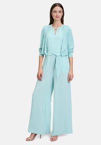 Lichtblauwe jumpsuit met een strik taille en geplooide halslijn, gecombineerd met een bijpassende open voorkardigan. Gladde stof en wijde pijpen.