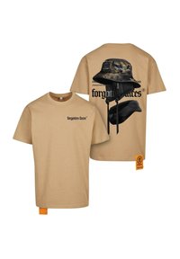 Beige bomulds T-shirt med frontlogo og ryggrafik af en sort bøttehat, der har camouflage-mønster og justerbare stropper, med et orange mærke.
