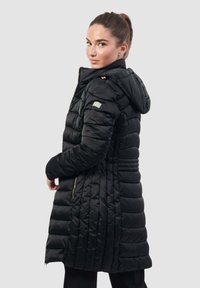Cappotto piumino nero con cappuccio, caratterizzato da un design trapuntato e dettagli in zip dorate. Presenta tasche laterali e una lunghezza maggiore per una migliore copertura.
