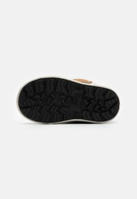 Semelle en caoutchouc noir avec un motif de semelle en zigzag, accentuée par une semelle intermédiaire de couleur claire. La tige présente un matériau marron près du talon.