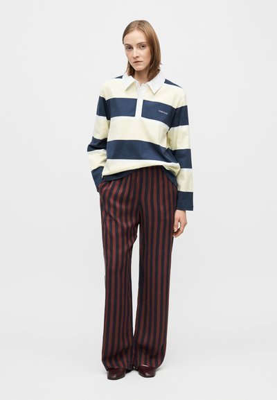 Tricou polo cu mânecă lungă în dungi albastre închise și galben pal, cu guler alb, asortat cu pantaloni largi cu dungi verticale bordo și albastre închise.